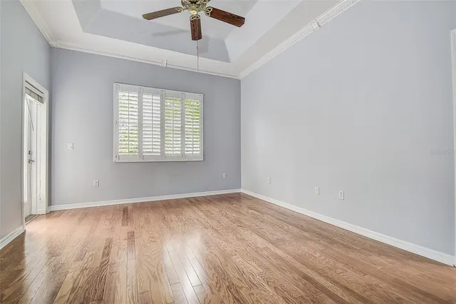 an empty room with wooden floor chandelier fan and windows