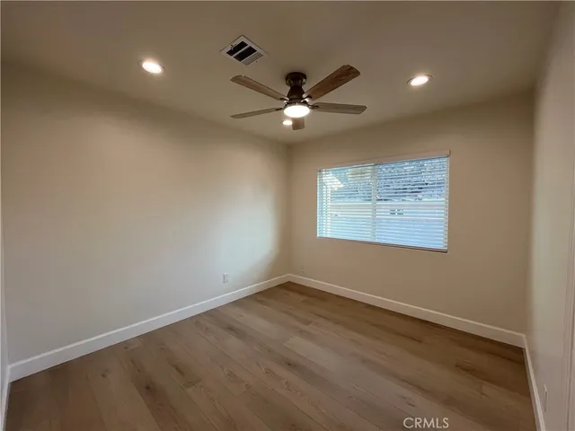 an empty room with wooden floor ceiling fan and windows