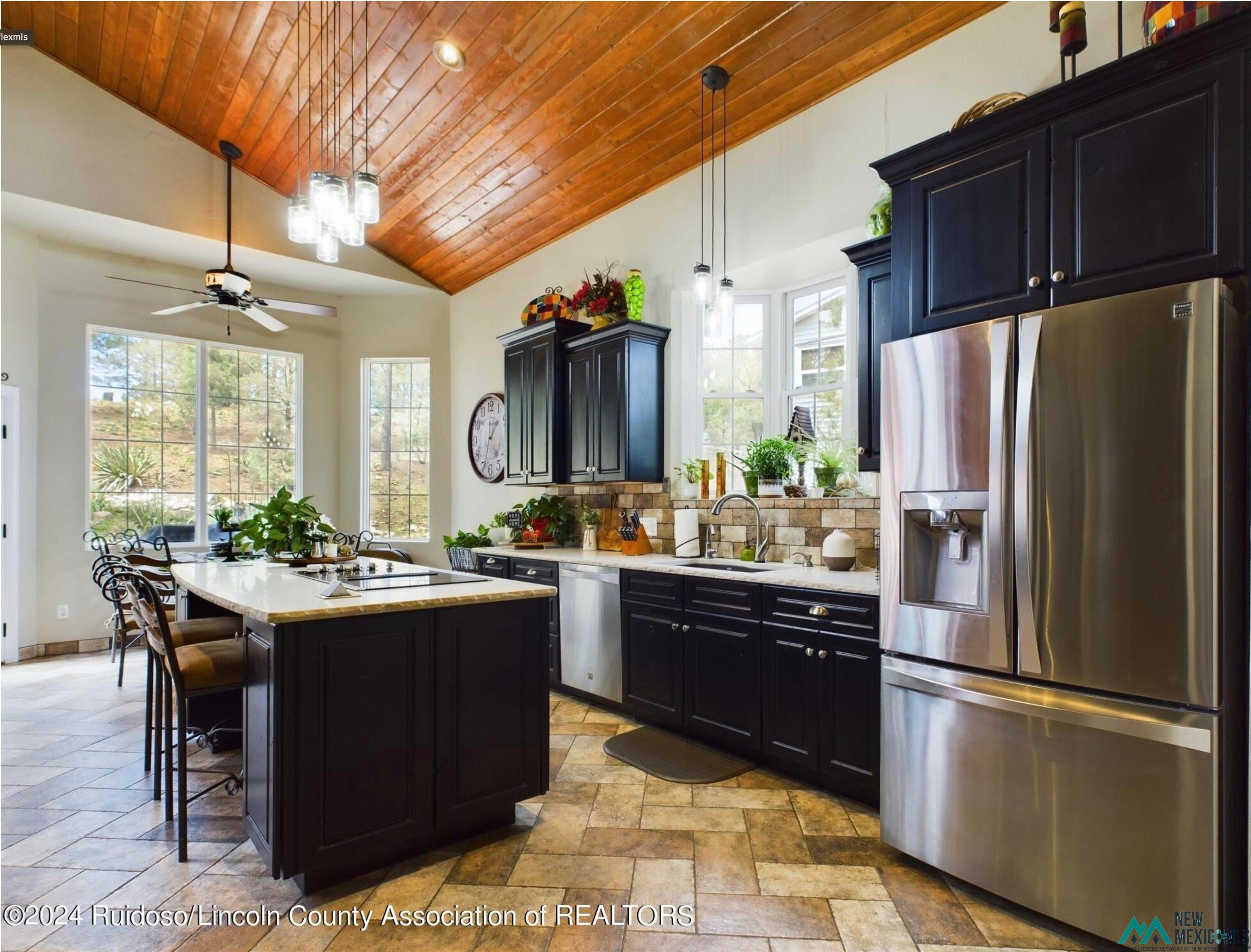 333 Ll Davis Drive Ruidoso, NM 88345 - Photo 11 of 25 Kitchen featuring a wood plank vaulted ceiling, a large center island with counter seating, stainless steel appliances, dark cabinetry, and multiple windows