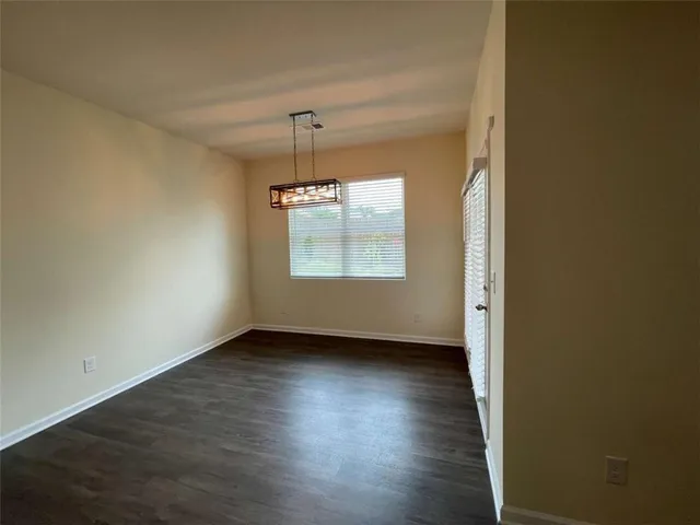 an empty room with wooden floor chandelier and windows