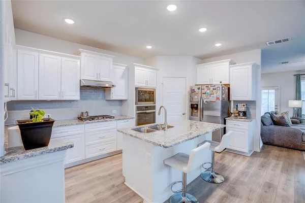 a kitchen with stainless steel appliances kitchen island granite countertop a refrigerator oven a stove a sink a dining table and chairs with wooden floor
