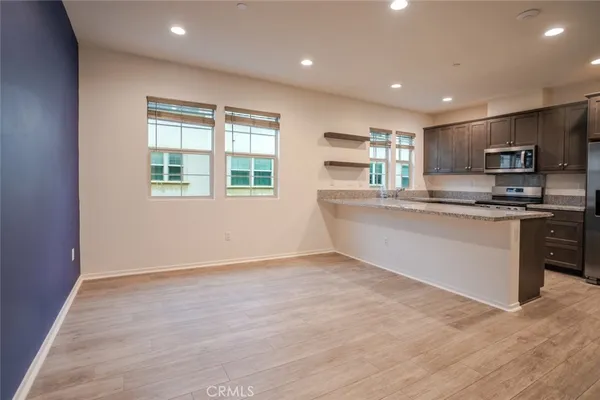 a large kitchen with stainless steel appliances granite countertop a stove a sink a refrigerator white cabinets and a wooden floor