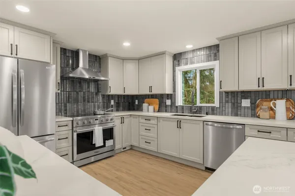 a kitchen with stainless steel appliances granite countertop a stove a sink dishwasher a refrigerator and white cabinets with wooden floor