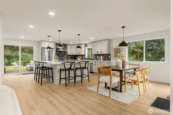 a open dining room with stainless steel appliances furniture wooden floor and a kitchen view