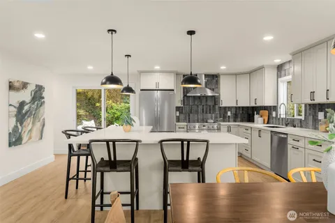 a kitchen with stainless steel appliances granite countertop a stove a refrigerator a kitchen island a dining table and chairs with wooden floor