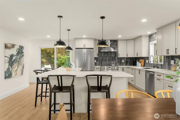 a kitchen with stainless steel appliances granite countertop a stove a refrigerator a kitchen island a dining table and chairs with wooden floor