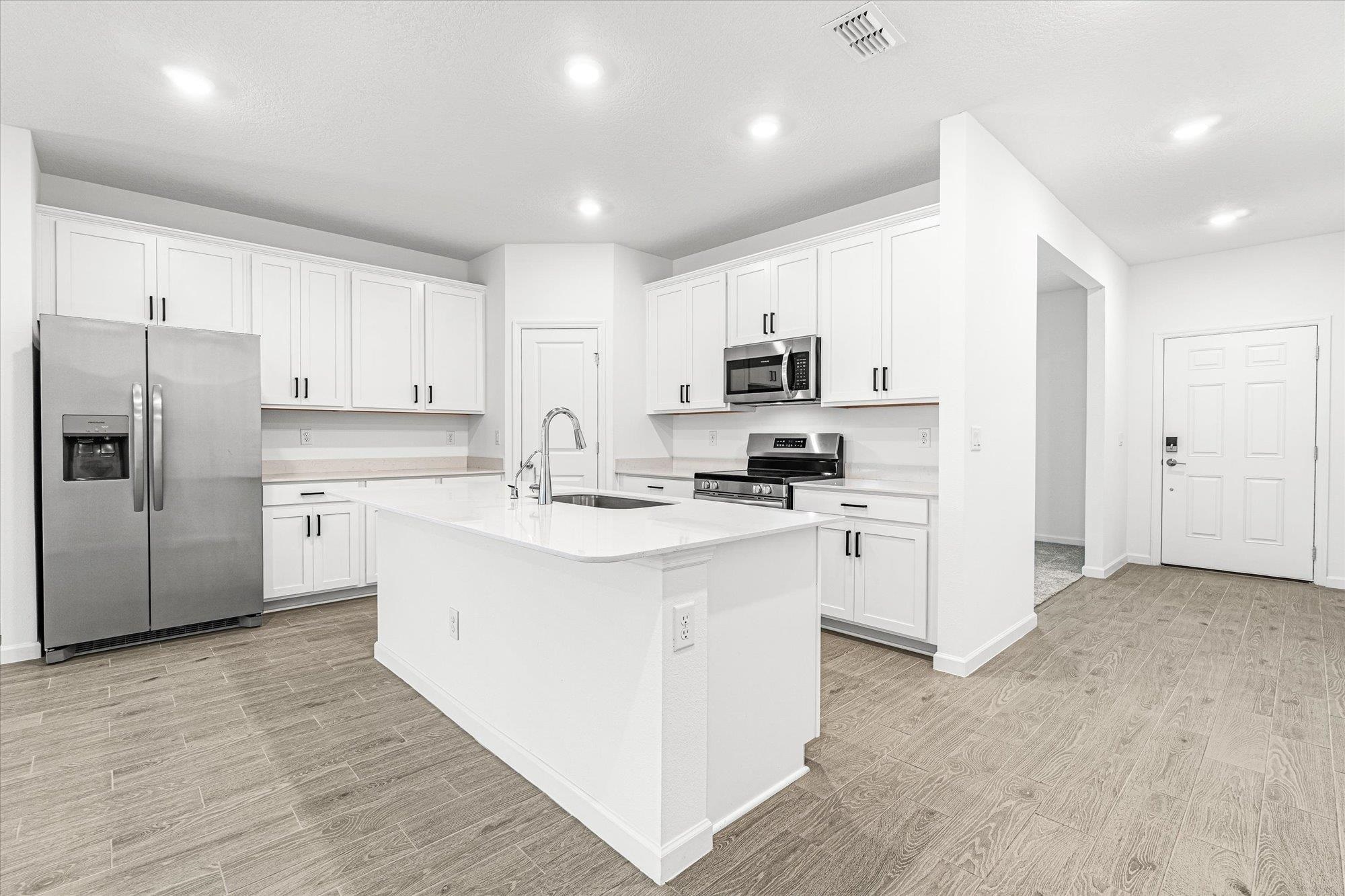 89 Kingsley Pk Way St. Augustine, FL 32084 - Photo 6 of 67 Kitchen featuring stainless steel appliances, wood finish floors, white cabinetry, an island with sink, and light stone countertops