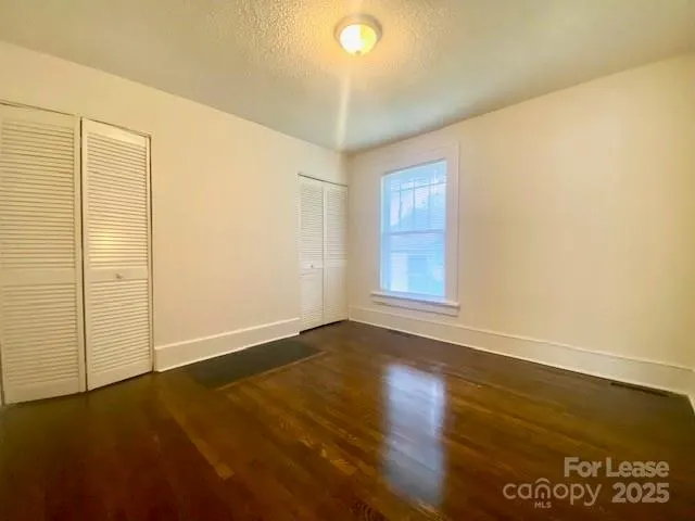 an empty room with wooden floor and windows with curtains