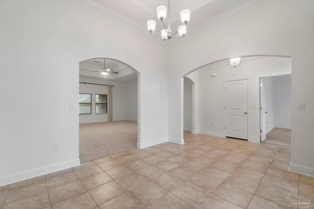 an empty room with a chandelier fan and kitchen view