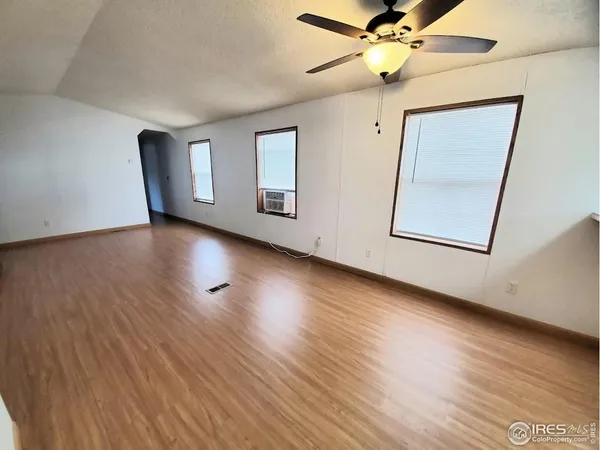 a view of an empty room with wooden floor and a ceiling fan