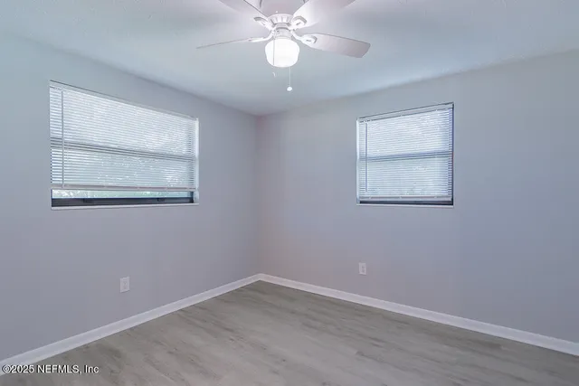 a view of an empty room with wooden floor and a chandelier fan