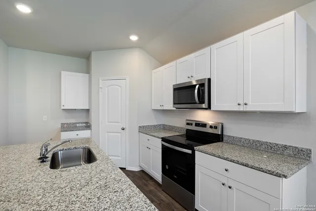 a kitchen with granite countertop a sink dishwasher stove and white cabinets