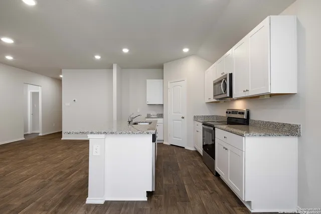 a kitchen with stainless steel appliances a stove top oven a sink a refrigerator white cabinets and wooden floor