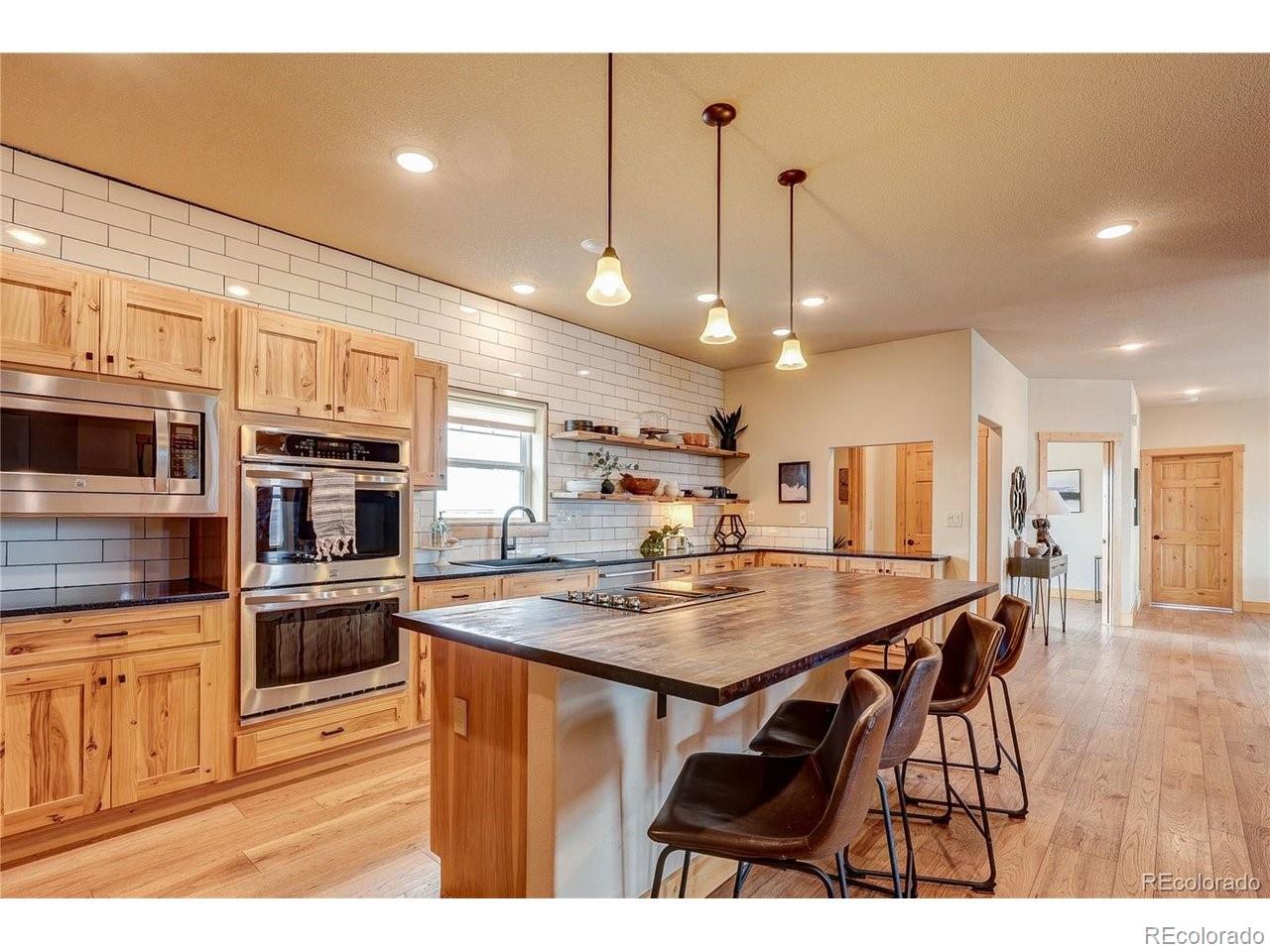 18298 Romar Rnch Road Carr, CO 80612 - Photo 13 of 49 a kitchen with stainless steel appliances kitchen island granite countertop a stove top oven a sink a dining table and chairs with wooden floor