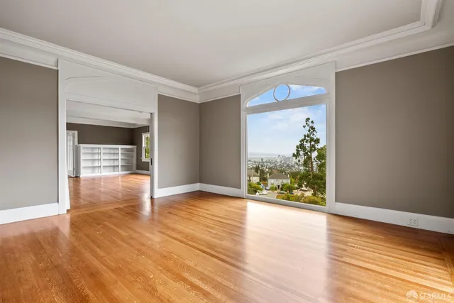 a view of an empty room with wooden floor fire place and a window