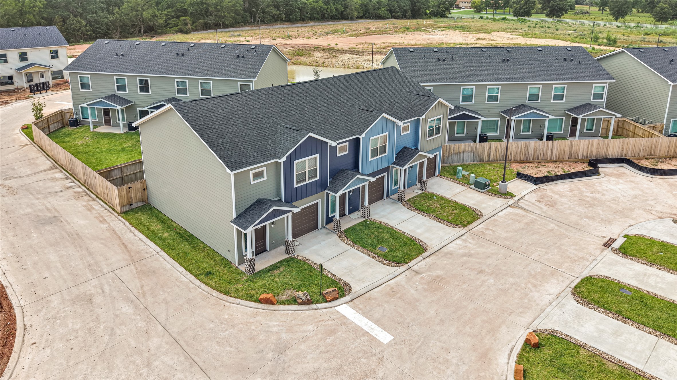 14010 Longstreet Road, Unit 2 Willis, TX 77318 - Photo 4 of 29 This photo shows a modern townhouse complex with multiple units, featuring two-story buildings with a clean, contemporary design. The homes have dark roofs, light siding, and small front yards. The area appears well-maintained, with paved roads and sidewalks.