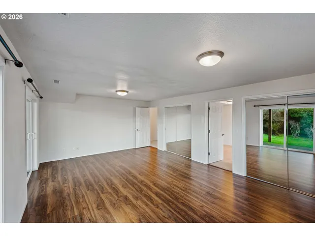 a view of an empty room with wooden floor and fan