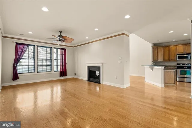 a view of an empty room with wooden floor and a kitchen