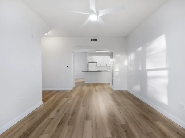 a view of empty room with wooden floor and kitchen