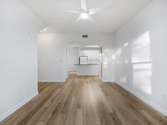 a view of empty room with wooden floor and kitchen