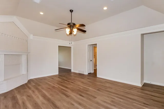 a view of an empty room with wooden floor and a ceiling fan