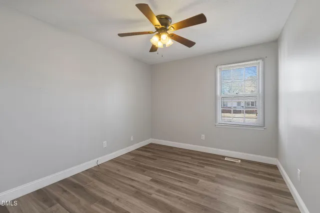 an empty room with wooden floor fan and windows