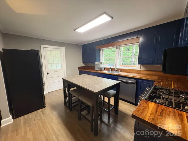 a kitchen with stainless steel appliances granite countertop a stove a refrigerator a sink a dining table and chairs with wooden floor