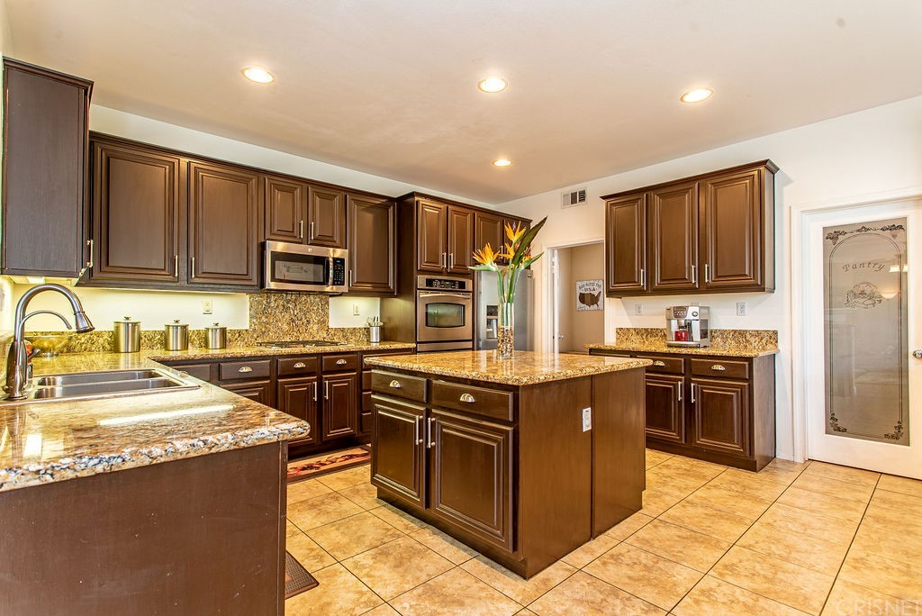 25054 Oliver Way Stevenson Ranch, CA 91381 - Photo 12 of 53 a kitchen with stainless steel appliances granite countertop a stove top oven a sink dishwasher a refrigerator and cabinets with wooden floor