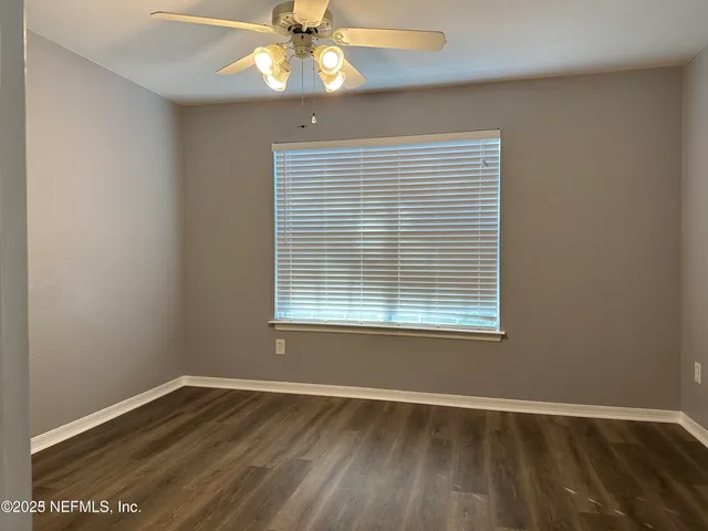 an empty room with wooden floor and way to kitchen