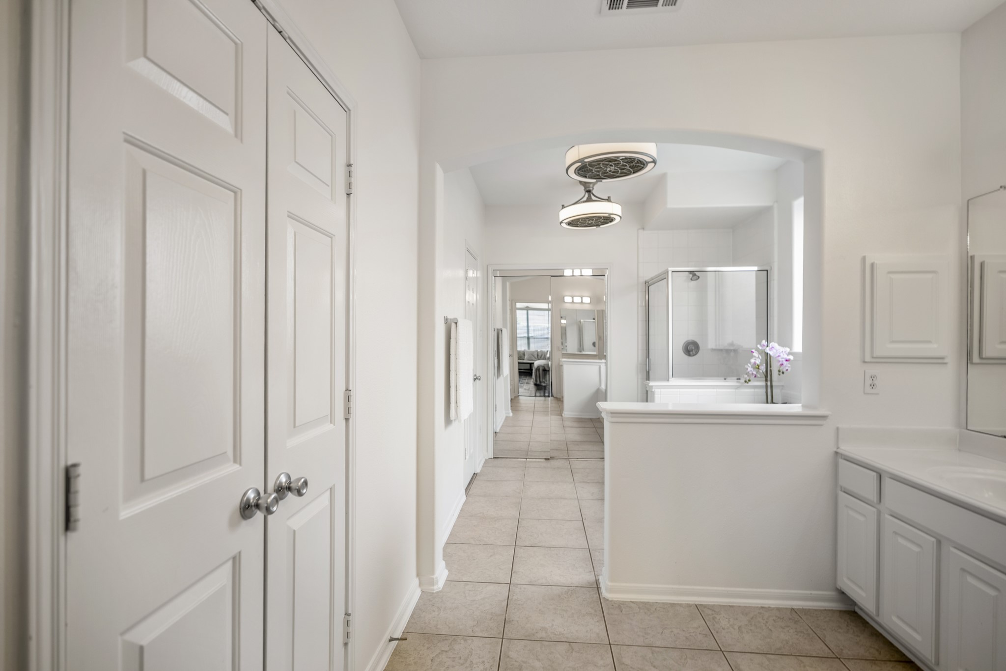 19106 South Rim Trail Spring, TX 77388 - Photo 23 of 50 Facing deeper into the primary bath, the layout shows how much space there is to move through the morning routine without feeling crowded. Double doors along the left add enclosed closet/storage access, while the arched opening draws you toward the soaking tub and separate shower. The vanity continues on the right, giving the suite a practical, easy flow from bedroom to bath to getting-ready space.