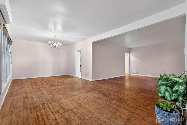 a view of an empty room with wooden floor and a chandelier