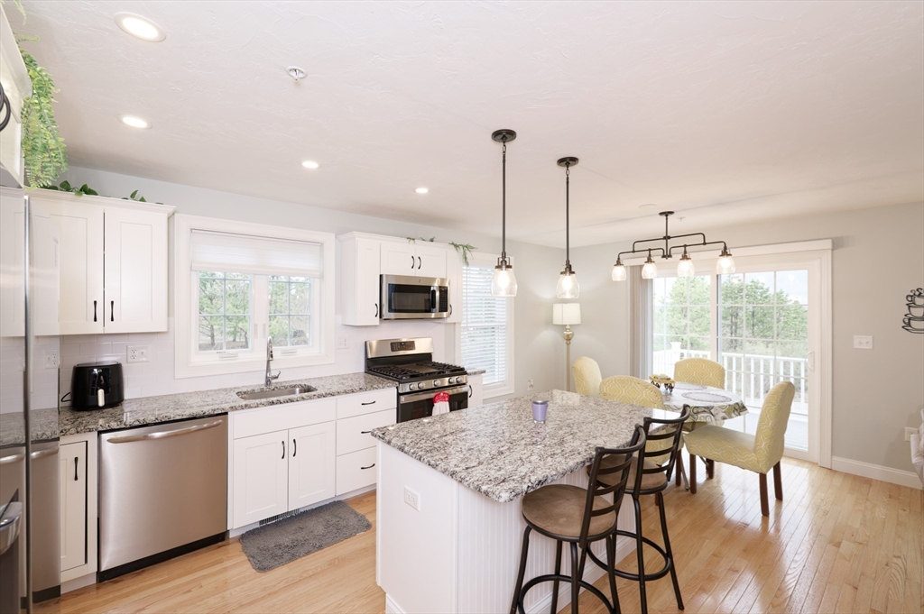 1202 Hazelwood Way, Unit 1202 Clinton, MA 01510 - Photo 9 of 38 a kitchen with stainless steel appliances kitchen island granite countertop a stove top oven a sink a dining table and chairs with wooden floor