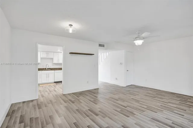 a view of empty room with wooden floor and kitchen