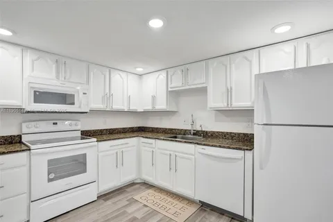 a kitchen with granite countertop white cabinets and white appliances