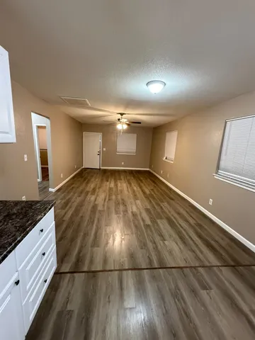 an empty room with wooden floor chandelier fan and windows