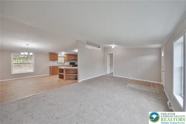 a view of an empty room with kitchen and window