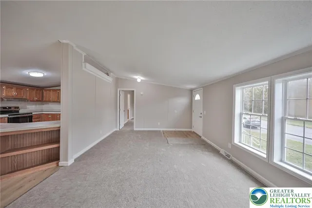 a view of an empty room with kitchen and window
