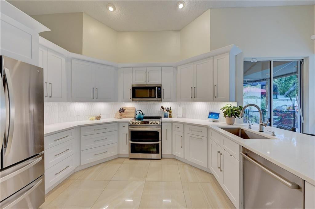 8171 Hampton Wood Drive Boca Raton, FL 33433 - Photo 54 of 56 a kitchen with white cabinets and stainless steel appliances