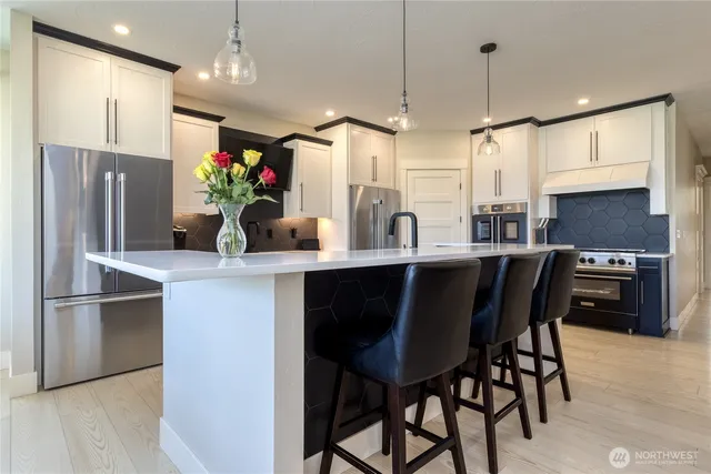 a kitchen with stainless steel appliances granite countertop a refrigerator a sink a stove and chairs with wooden floor