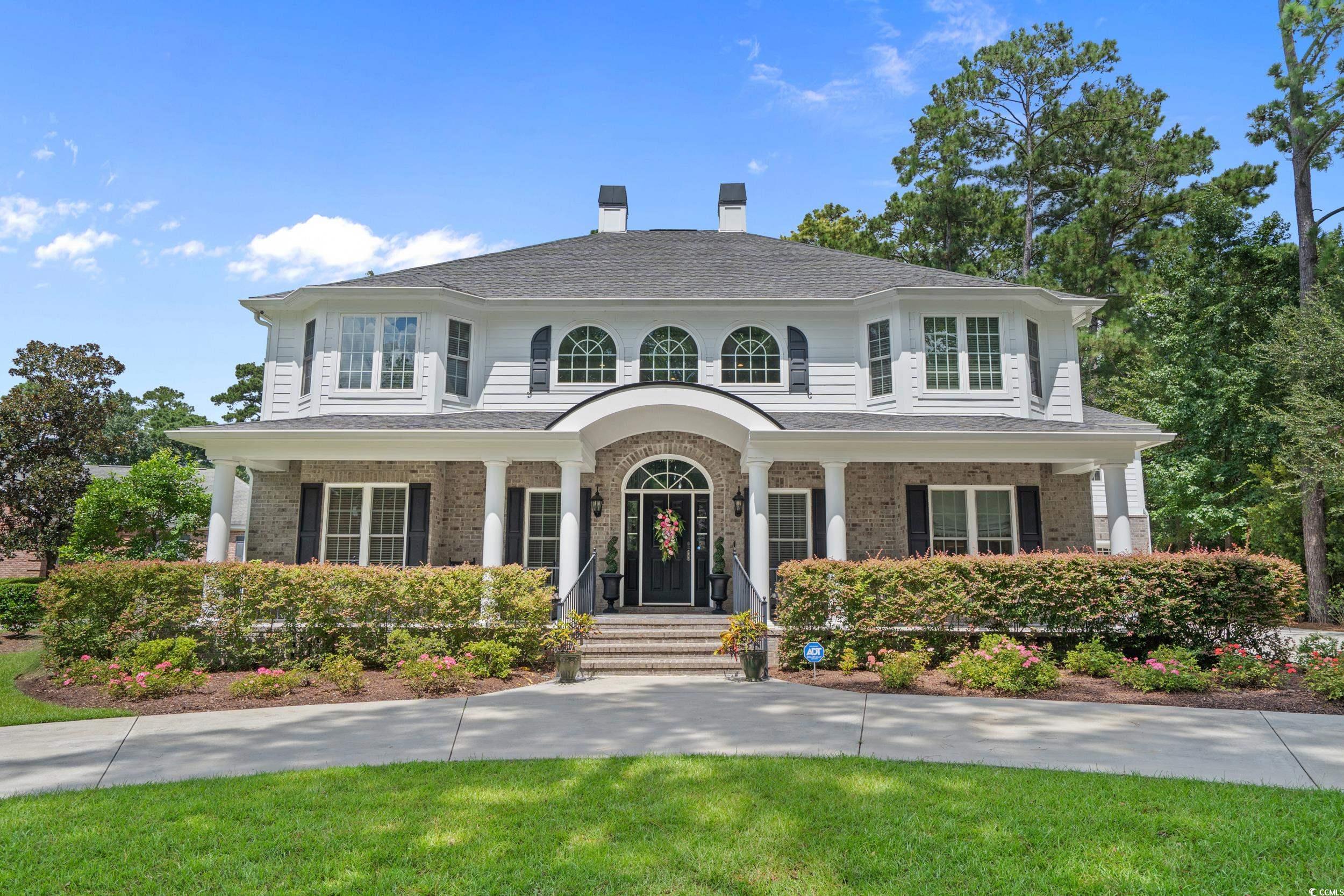 View of front of house with a chimney, covered porch, brick siding, and roof with shingles