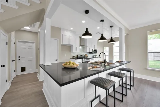 a kitchen with stainless steel appliances granite countertop a stove top oven a sink a refrigerator and white cabinets with wooden floor