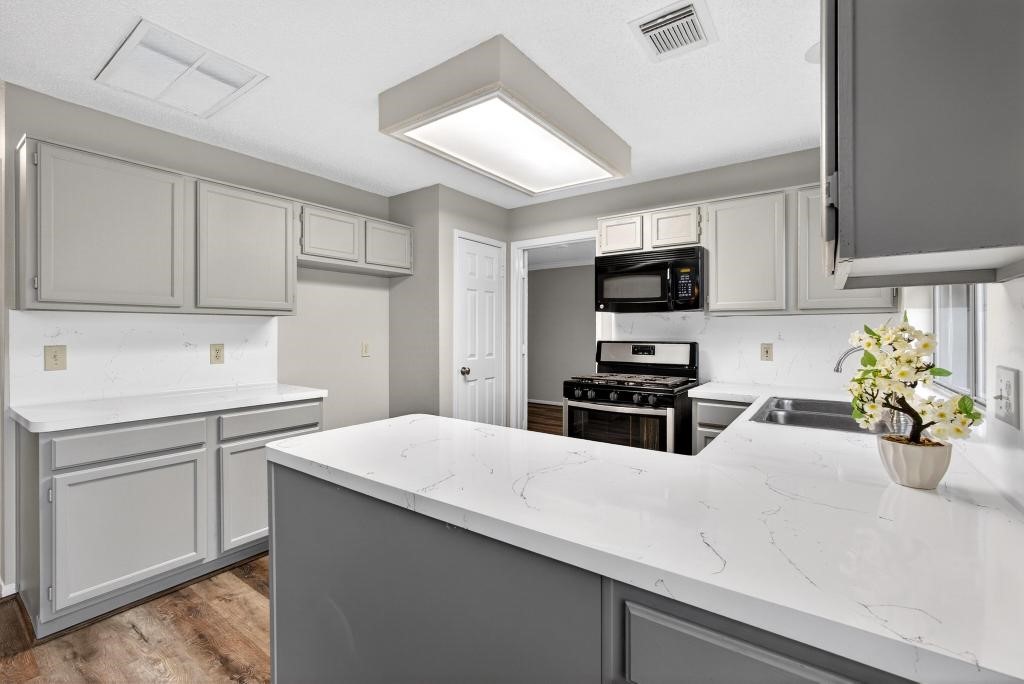 8815 Stoney Bend Drive Spring, TX 77379 - Photo 10 of 50 This kitchen features modern cabinetry, sleek white countertops, and a gas range. It includes a built-in microwave, a dual-basin sink, and natural light from a window, creating a bright and functional space.