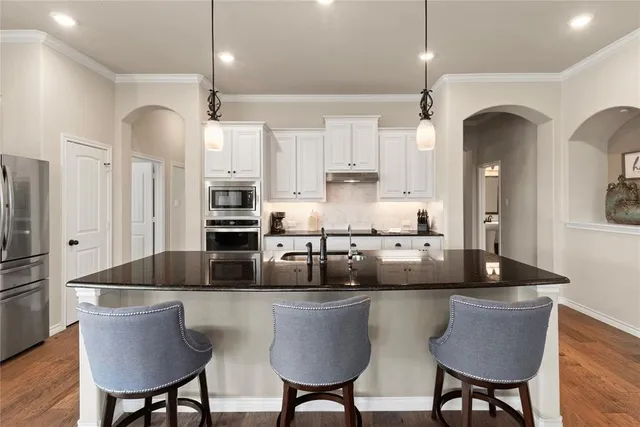 a kitchen with stainless steel appliances granite countertop a dining table chairs refrigerator and sink