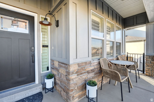 14738 Tangle Hill Road Herriman, UT 84096 - Photo 11 of 66 Covered front porch featuring stacked stone accents, vertical board and batten siding, multiple windows, and a panel-style entry door with a decorative glass insert
