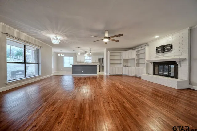 an empty room with wooden floor fireplace and windows