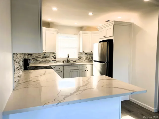 a kitchen with stainless steel appliances kitchen island granite countertop a refrigerator a sink a stove and white cabinets with wooden floor