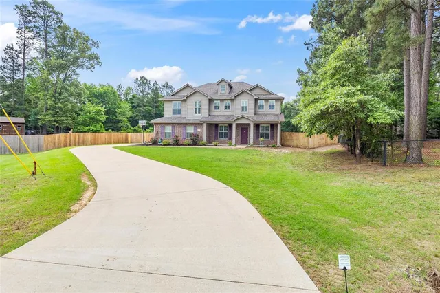 a view of a white house in front of a big yard with plants and large trees