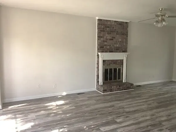 a view of an empty room with wooden floor fireplace and a window