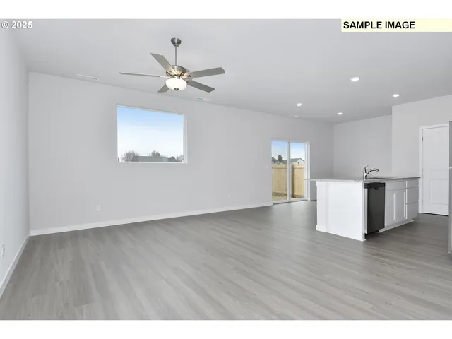 a view of an empty room with wooden floor and a ceiling fan