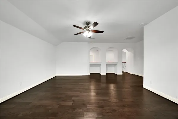 a view of an empty room with wooden floor ceiling fan and window
